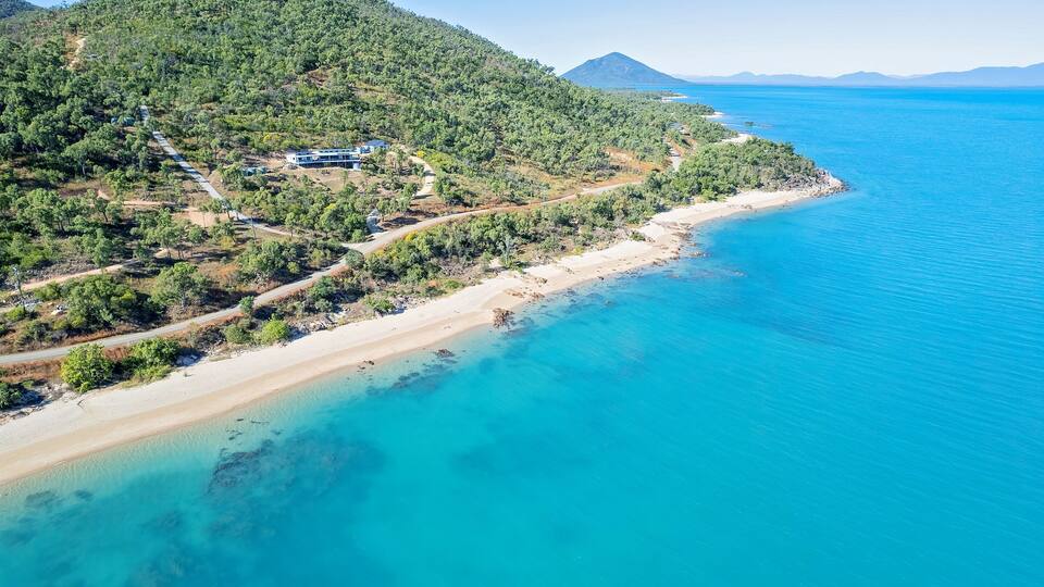 A coastal landscape with a sandy beach, clear turquoise waters, and a forested hillside.