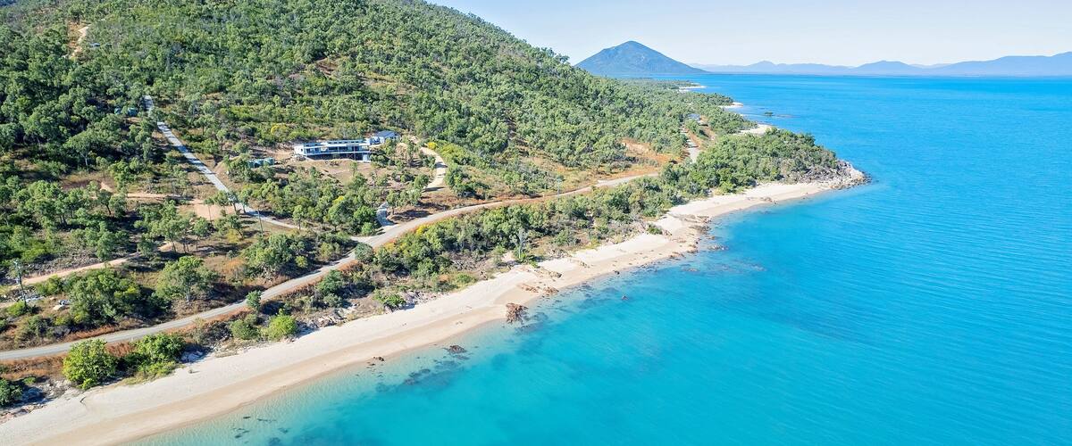 A coastal landscape with a sandy beach, clear turquoise waters, and a forested hillside.