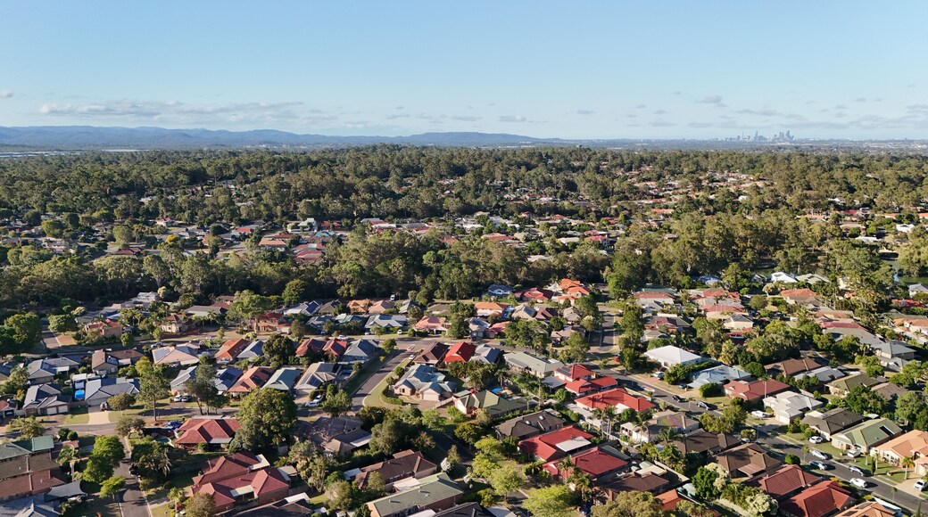 A residential area with houses, trees, and distant mountains under a clear sky.