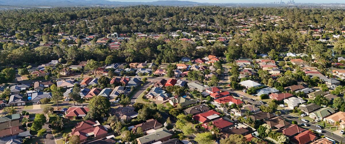 A residential area with houses, trees, and distant mountains under a clear sky.