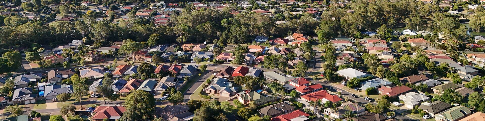 A residential area with houses, trees, and distant mountains under a clear sky.