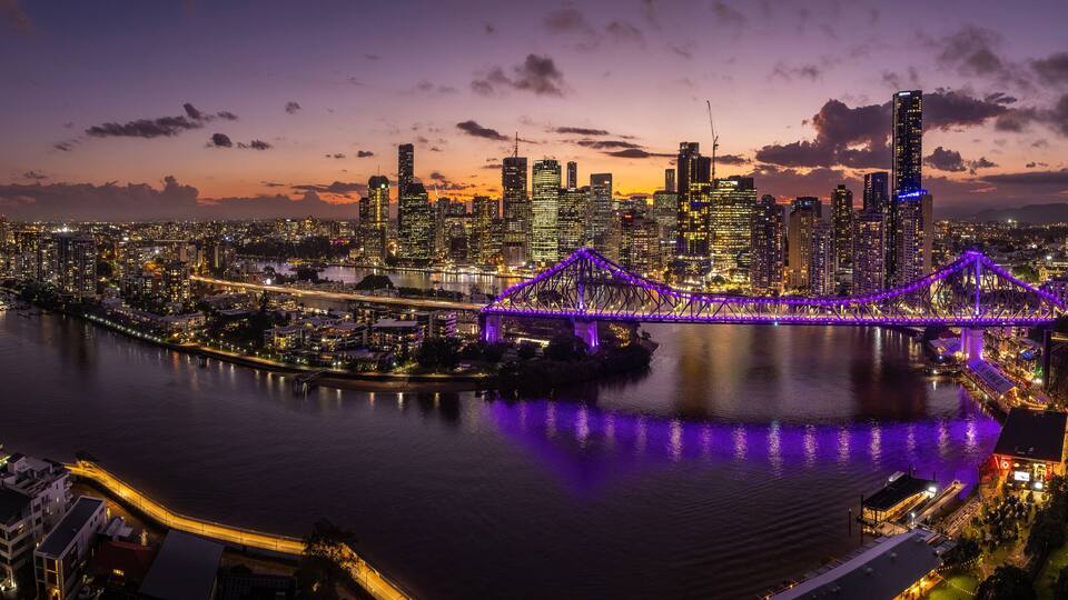Ein Stadtbild bei Dämmerung, mit einer markanten Brücke, die in violetten Lichtern erstrahlt.