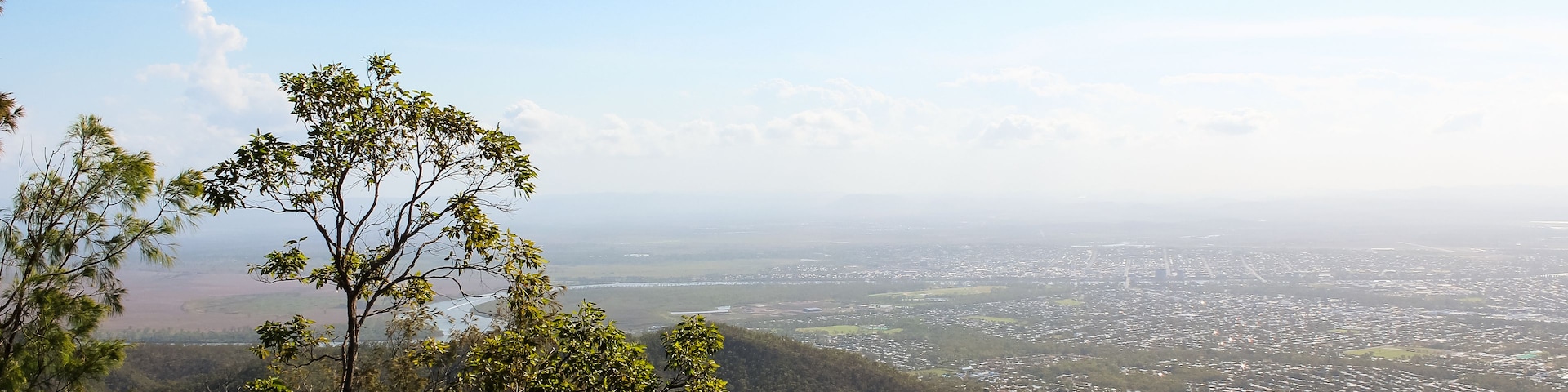 A mountainous landscape with dense greenery and a distant view of a cityscape.
