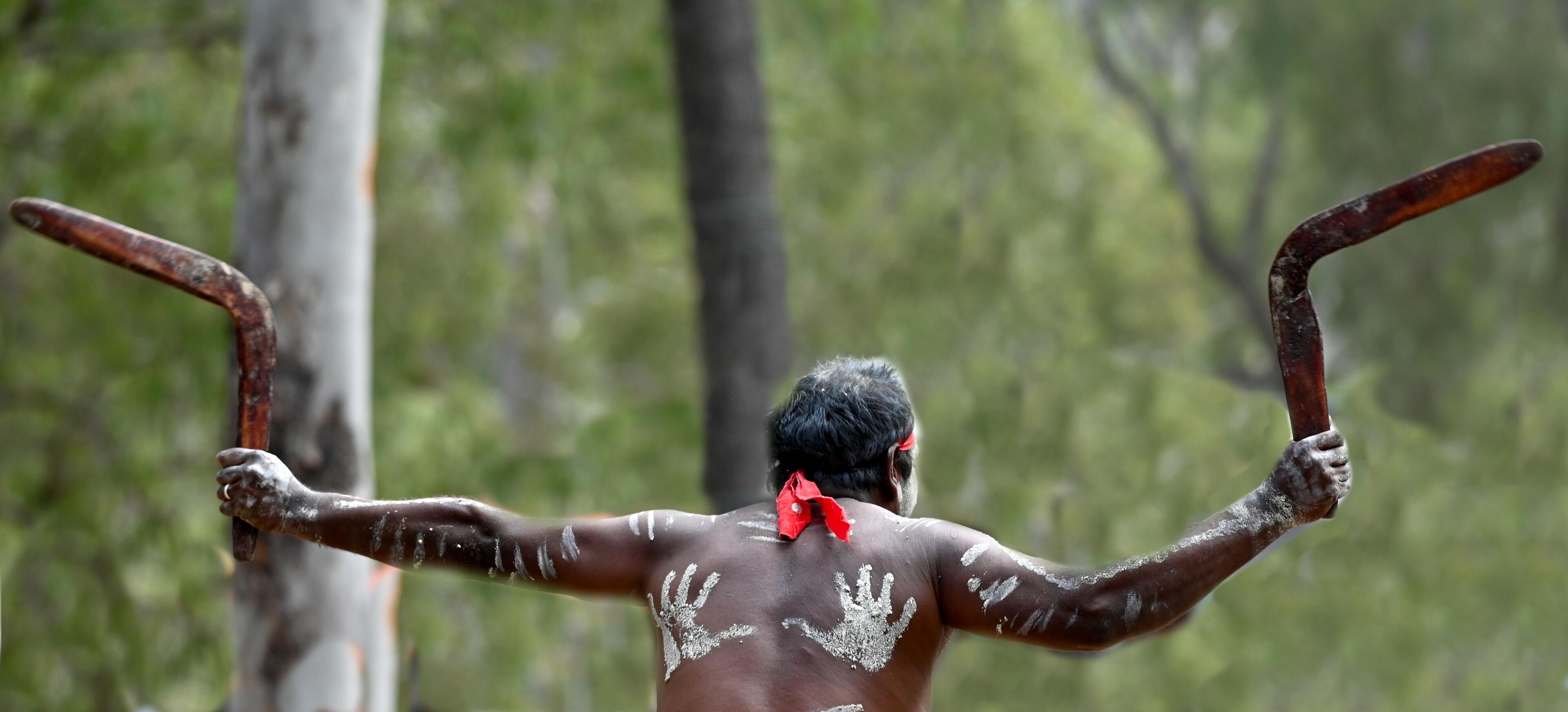 A person with white paint on their back and arms, holding two rusty objects.