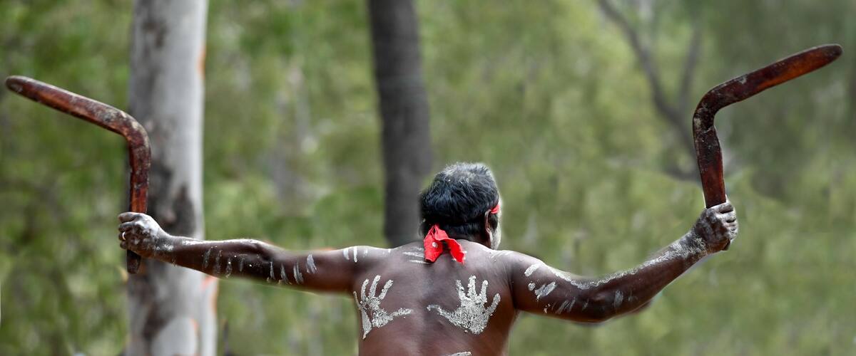 A person with white paint on their back and arms, holding two rusty objects.