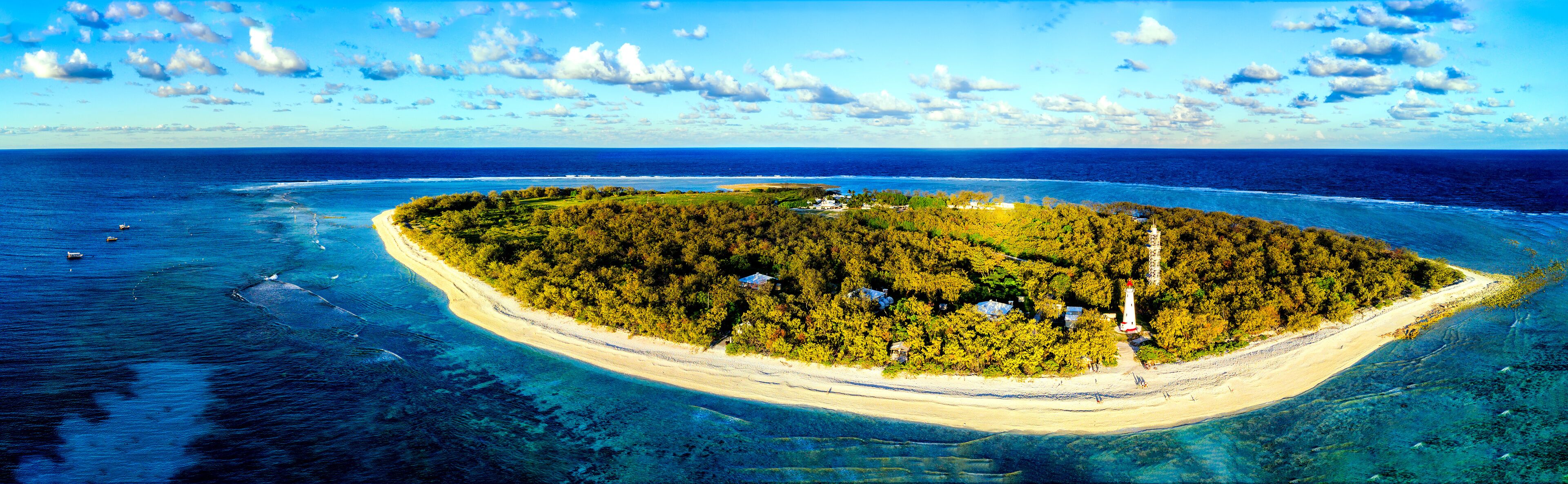 An island with a lighthouse, surrounded by clear blue waters and a sandy beach.