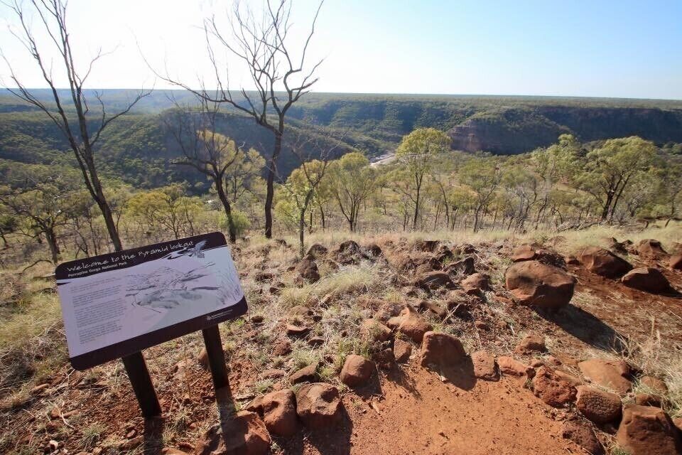 A signboard in a natural landscape with rocky terrain and sparse trees.