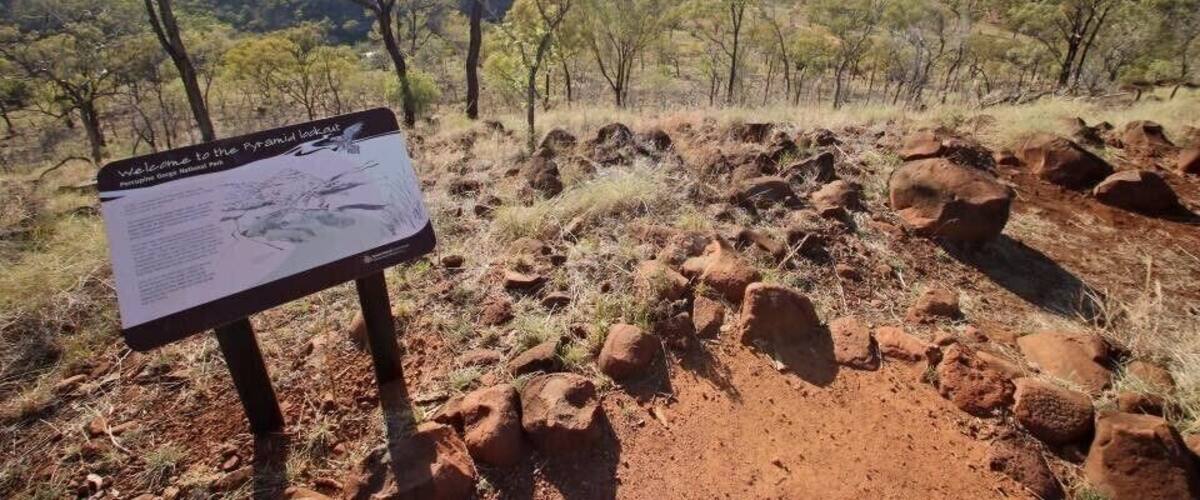 A signboard in a natural landscape with rocky terrain and sparse trees.