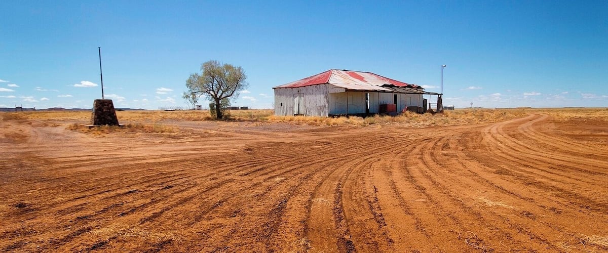 A rural landscape with a dirt road, a red-roofed barn, a solitary tree, and a utility pole.
