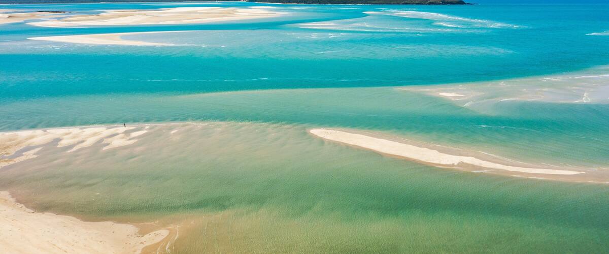 A coastal landscape with clear turquoise waters, sandy beaches, and distant hills.