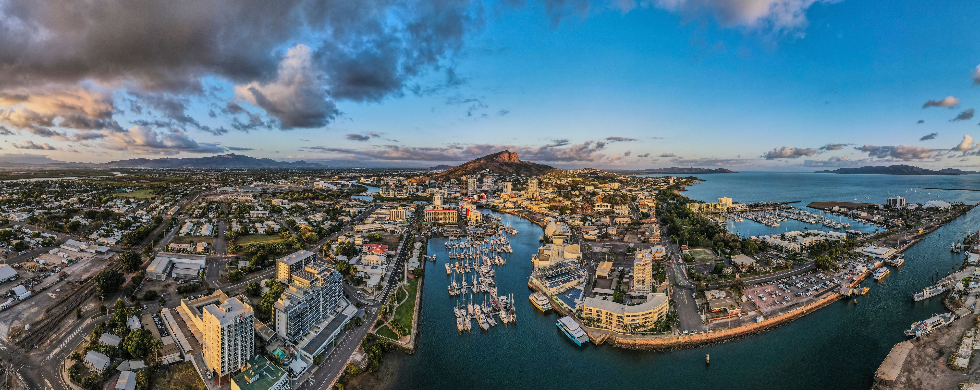 A coastal cityscape with a marina, buildings, and a prominent mountain.
