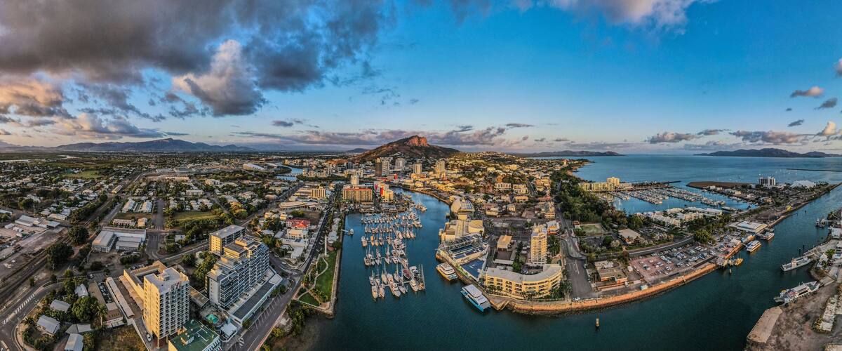Un paisaje urbano costero con un puerto deportivo, edificios y una montaña destacada.