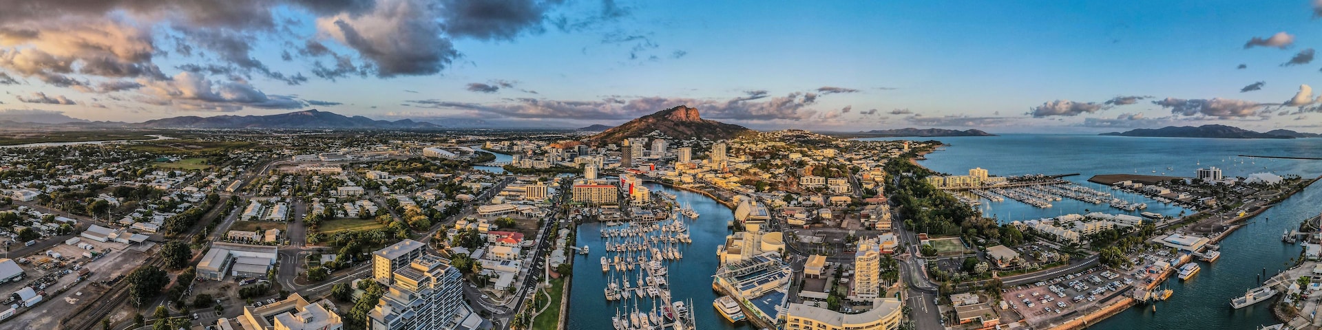 A coastal cityscape with a marina, buildings, and a prominent mountain.