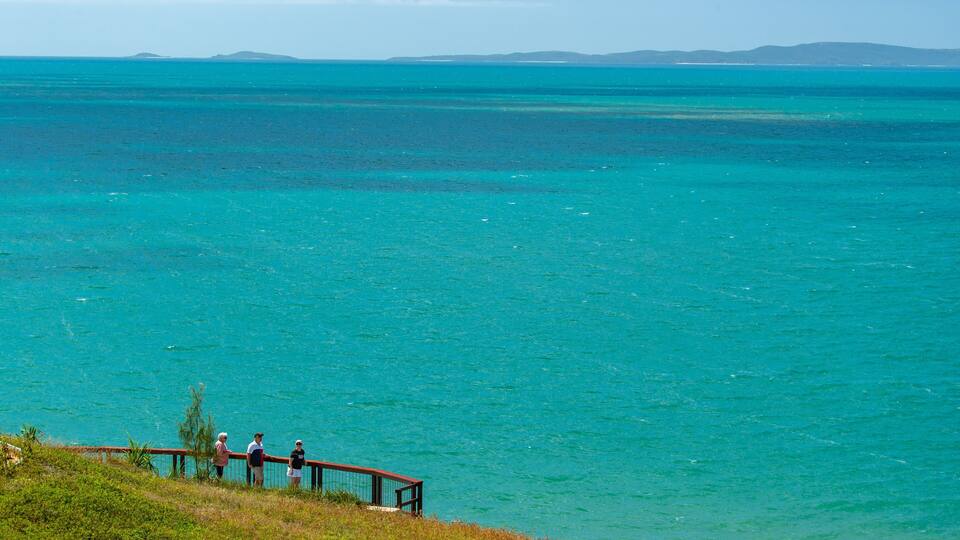 A coastal landscape with a clear turquoise sea, a wooden walkway, and distant islands.