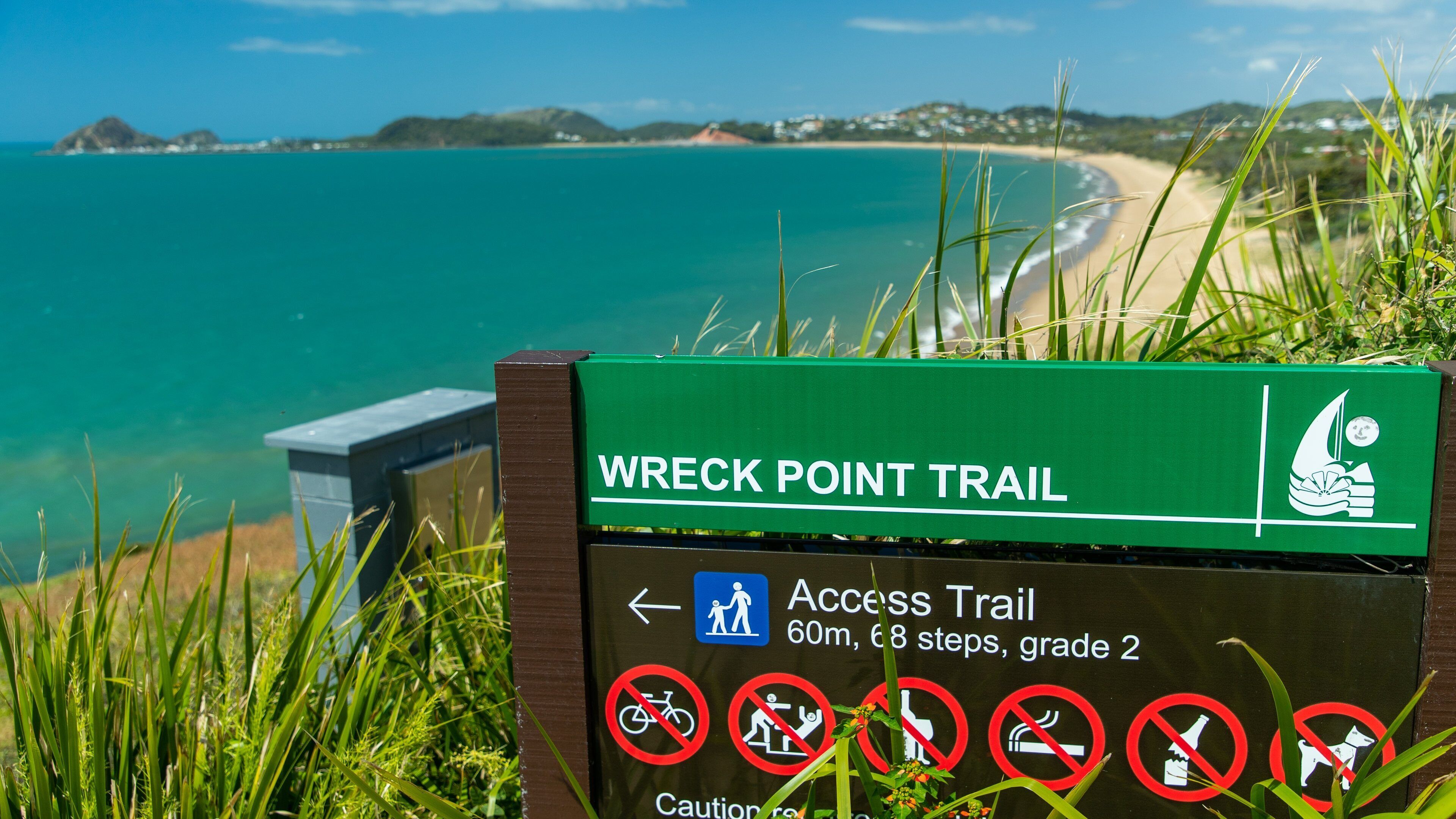 A sign for the Wreck Point Trail with a beach and ocean in the background.