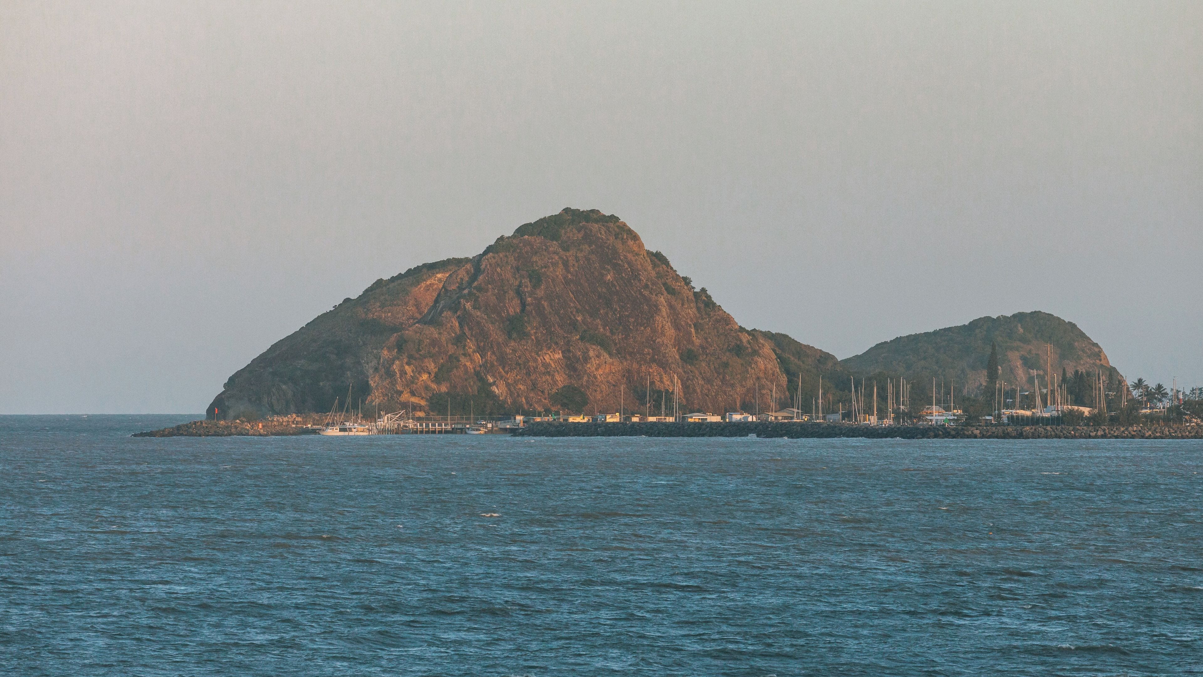 A coastal landscape with two prominent rocky hills and a marina with boats.