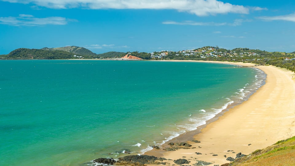 A turquoise beach with clear waters, sandy shore, and a hilly landscape in the background.