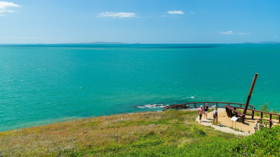 A coastal landscape with a clear view of turquoise waters, a wooden walkway, and a grassy area.