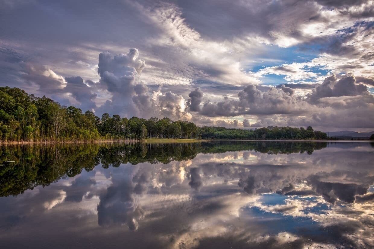 A calm lake reflecting clouds and trees.