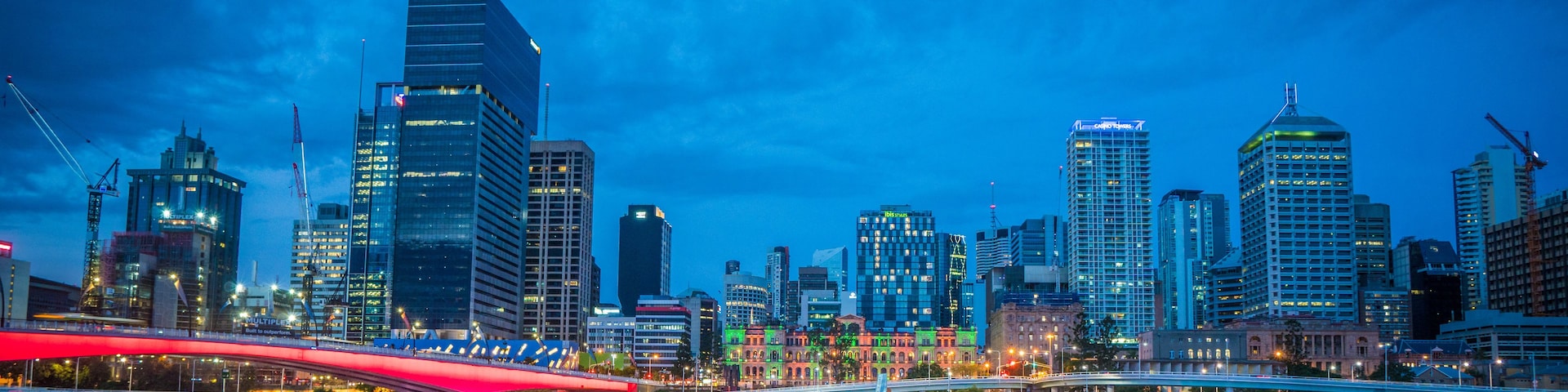 A city skyline at dusk with illuminated buildings and a red bridge over a river.