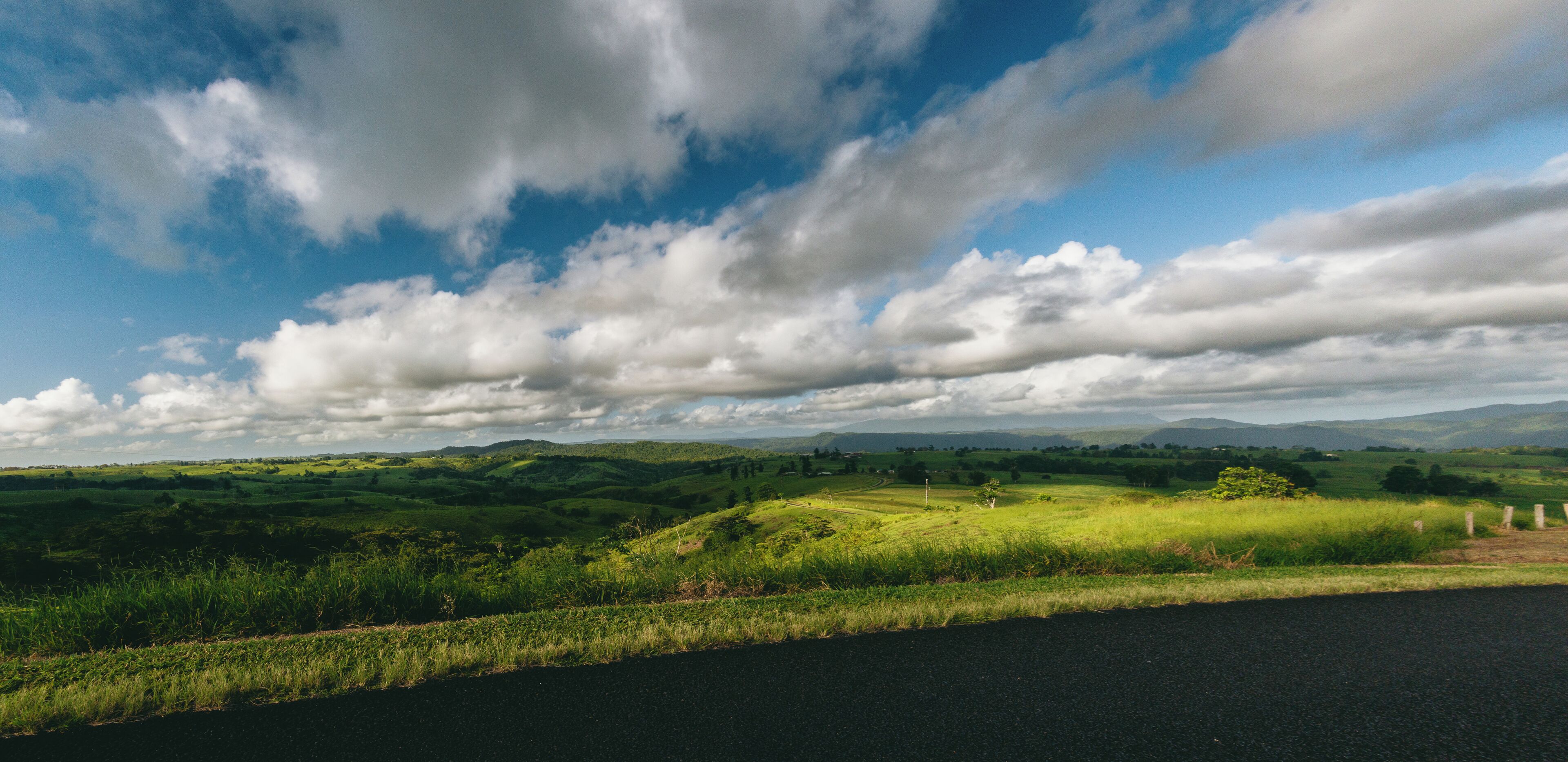 A rural landscape with rolling hills, a road, and a partly cloudy sky.