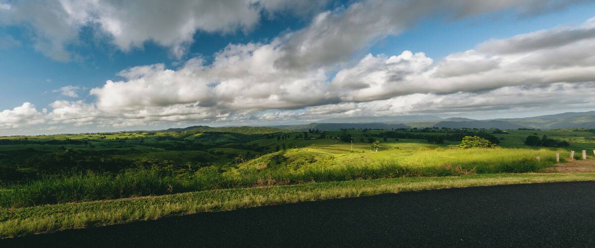 A rural landscape with rolling hills, a road, and a partly cloudy sky.