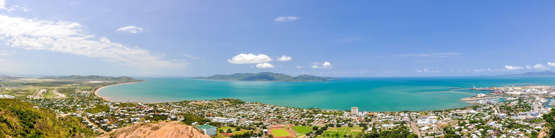 Uma vila costeira com uma baía, montanhas ao fundo e céu claro.