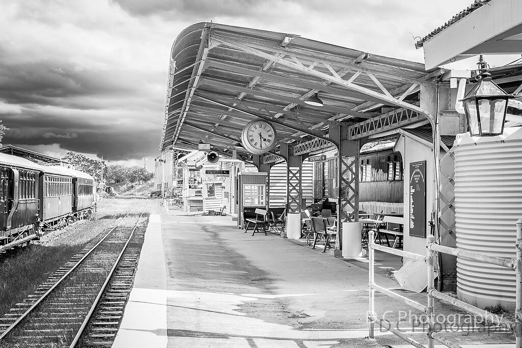 A train station with a covered waiting area, a clock, and a vintage lamp.
