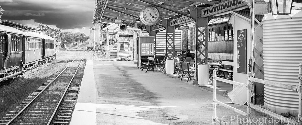 A train station with a covered waiting area, a clock, and a vintage lamp.