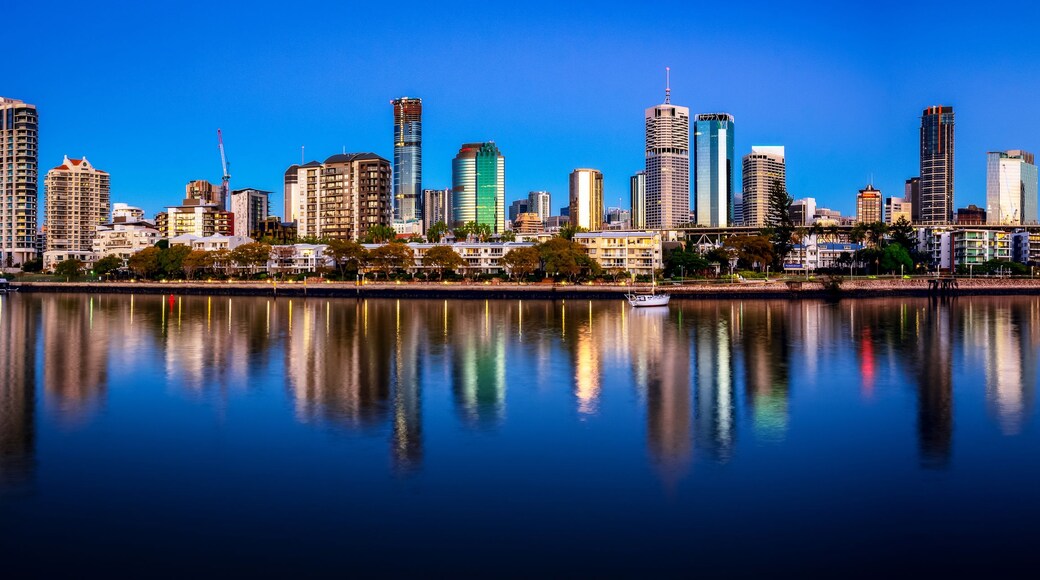 A city skyline with high-rise buildings and a bridge reflecting on the water.