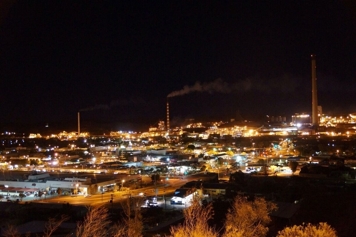A nighttime cityscape with industrial buildings and smokestacks emitting smoke.