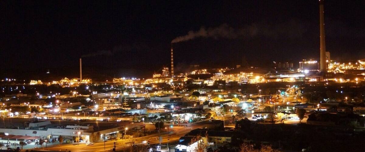 A nighttime cityscape with industrial buildings and smokestacks emitting smoke.