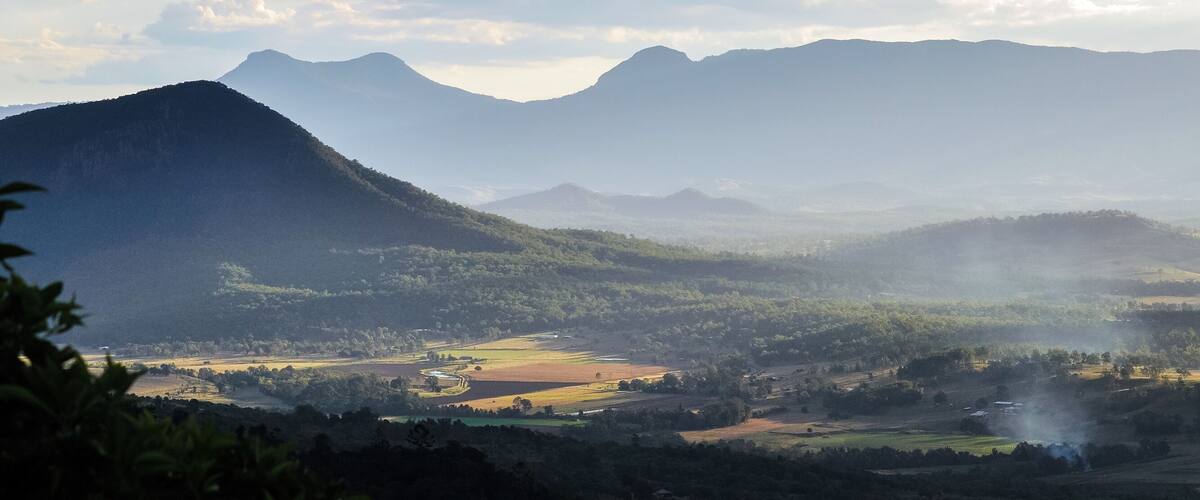 A mountainous landscape with rolling hills, a valley, and a distant mountain range under a partly cloudy sky.