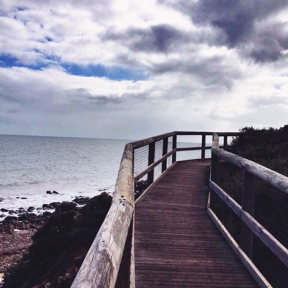 A wooden boardwalk leading to the ocean with a cloudy sky above.