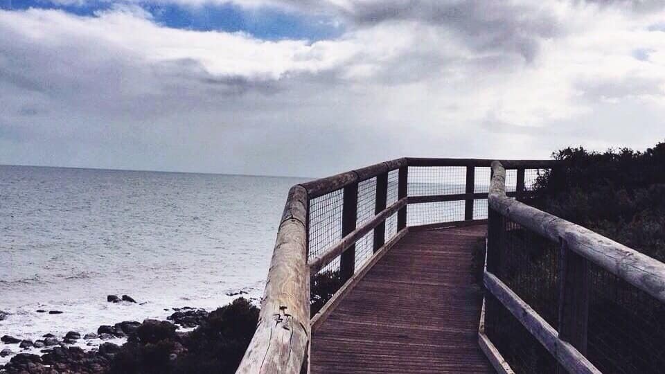 A wooden boardwalk leading to the ocean with a cloudy sky above.