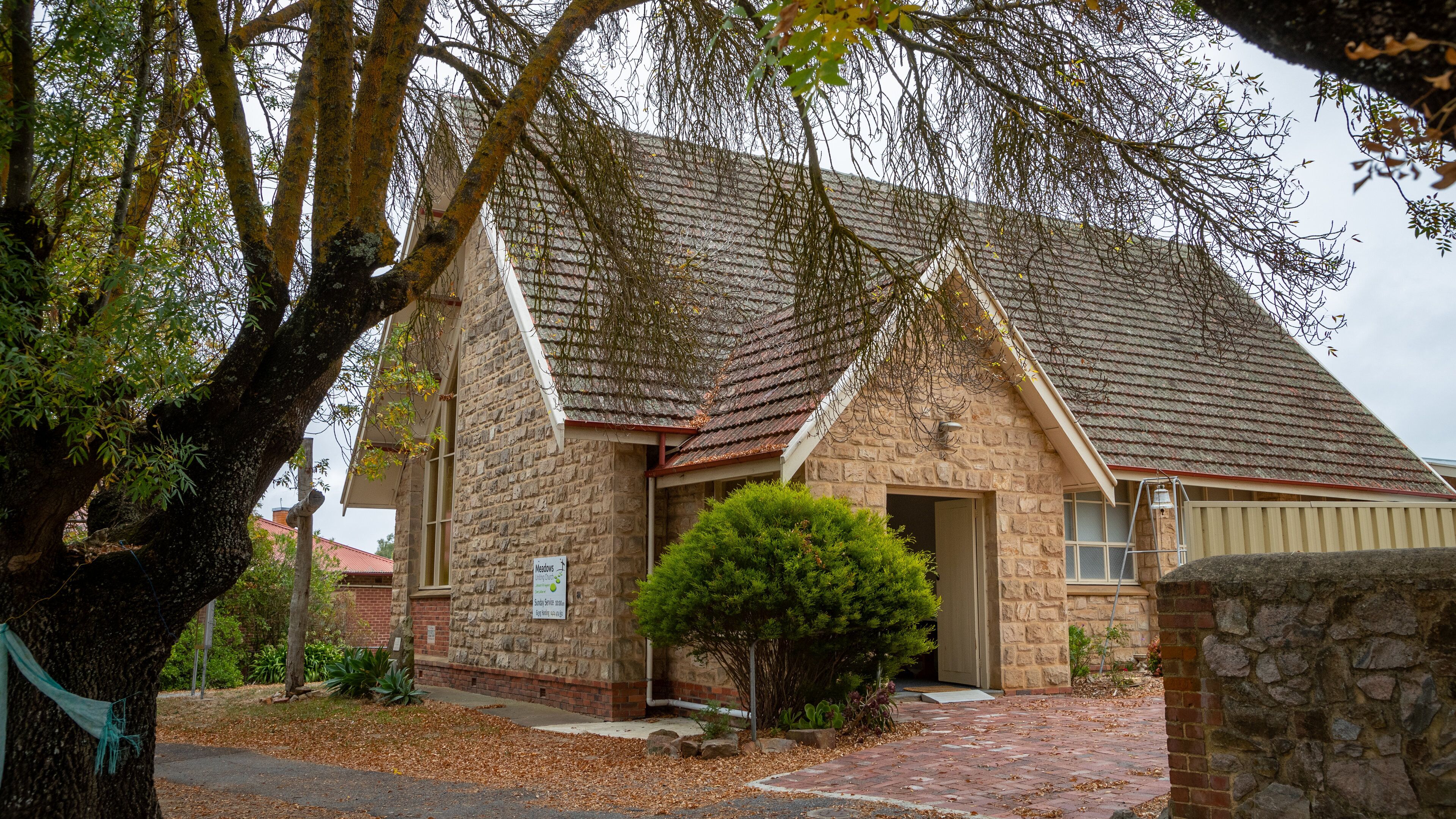 A stone building with a tiled roof, surrounded by trees and a brick pathway.
