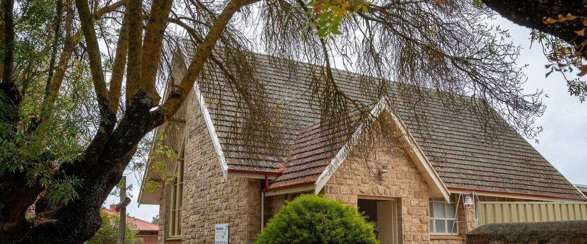 A stone building with a tiled roof, surrounded by trees and a brick pathway.