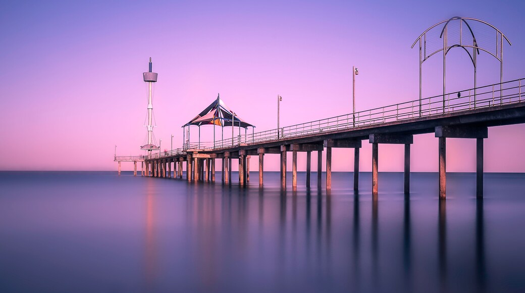 A pier extending into calm waters with a lighthouse and a covered structure.