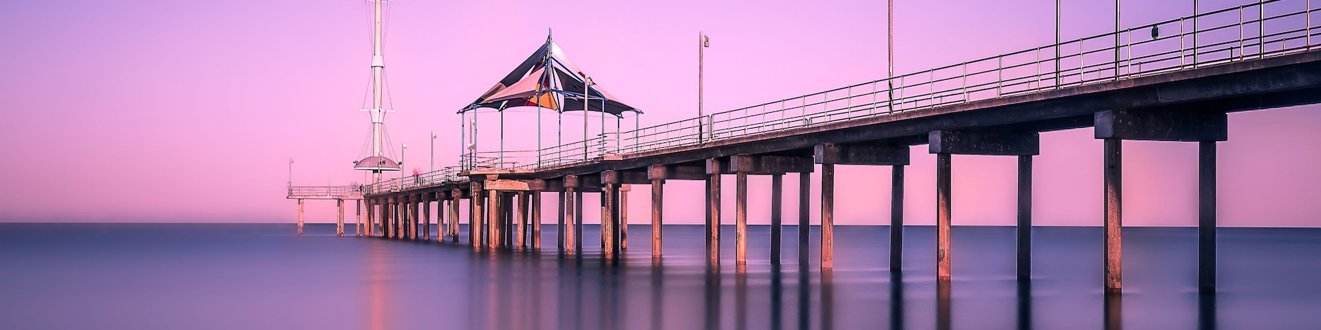 Un muelle se adentra en aguas tranquilas, con un faro y una estructura cubierta.