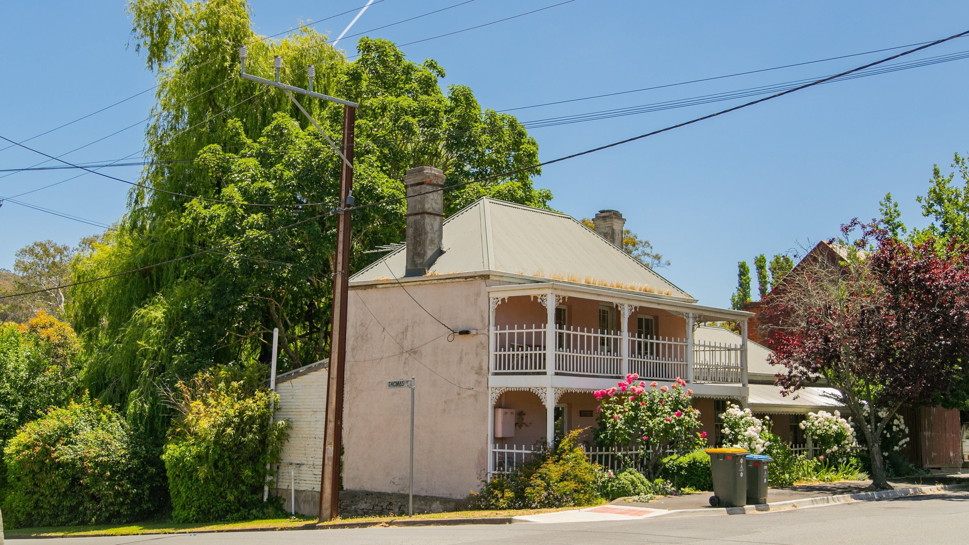 A two-story house with a porch, surrounded by lush greenery and flowering plants.