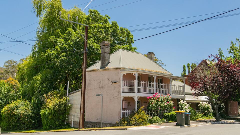 A two-story house with a porch, surrounded by lush greenery and flowering plants.