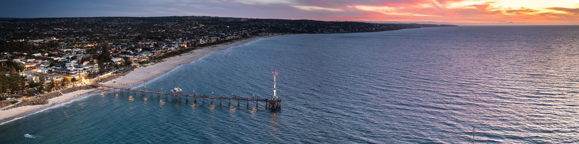 Un paisaje costero con un muelle que se adentra en el mar, un faro y un velero.