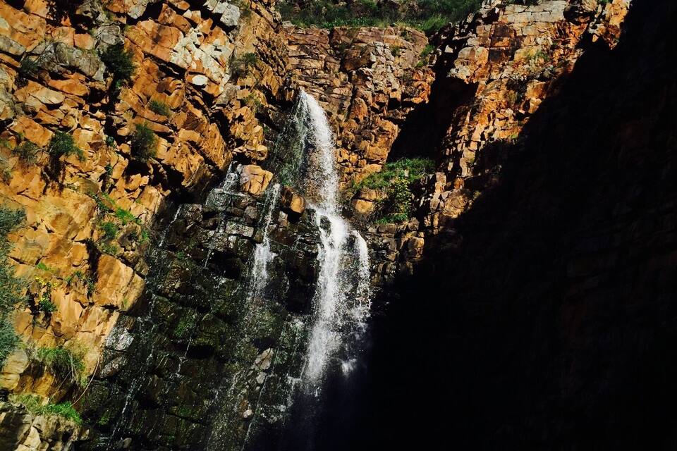 A waterfall cascading down a rocky cliff surrounded by greenery.