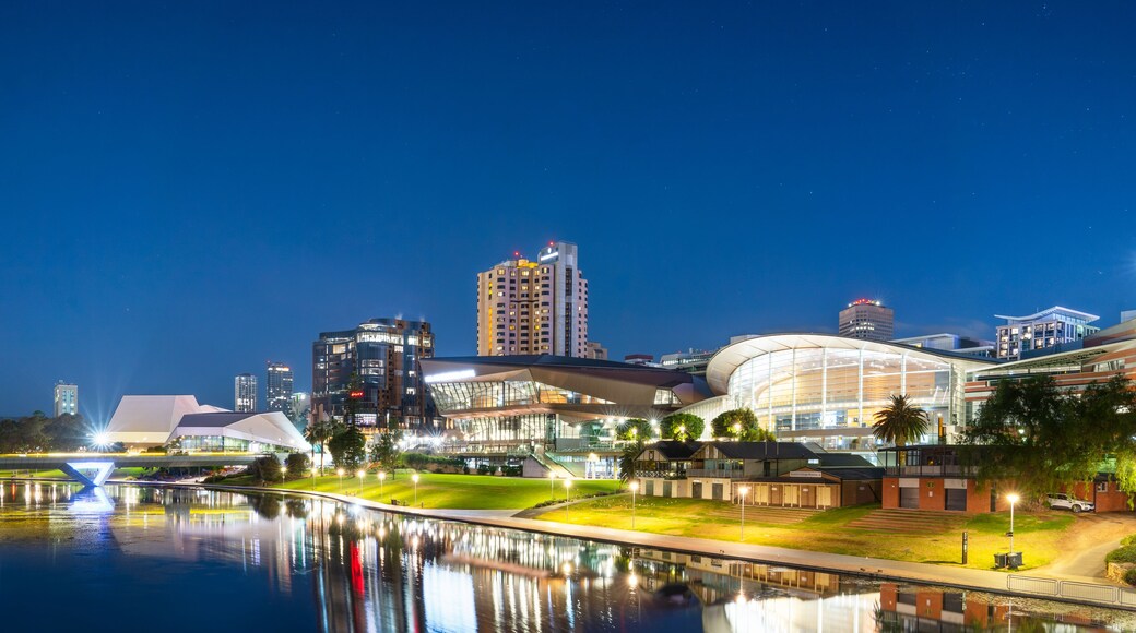 A cityscape at night with illuminated buildings, a reflective water body, and a modern architectural structure.
