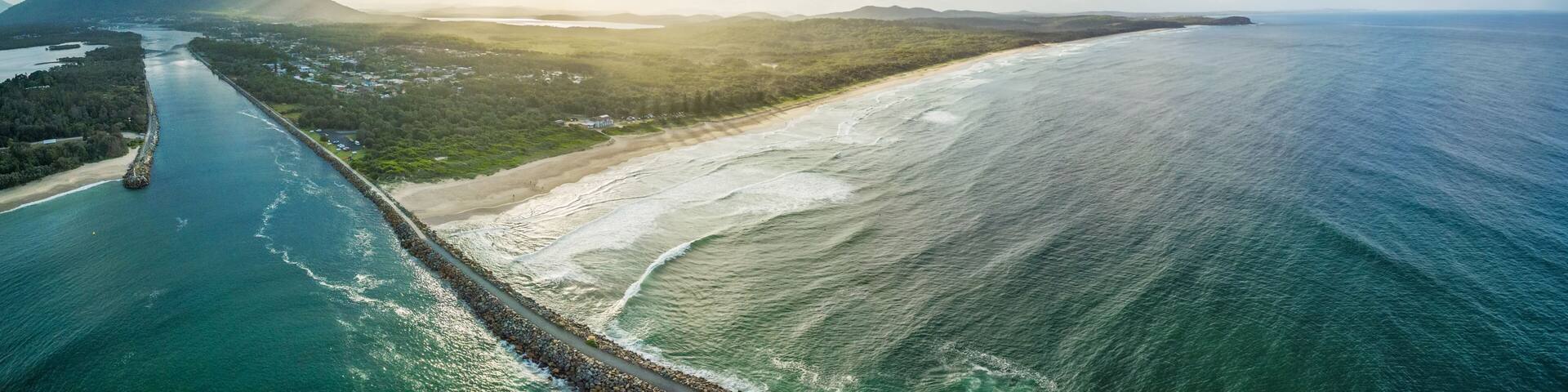 A coastal landscape with a beach, a pier, and a mountain in the distance.