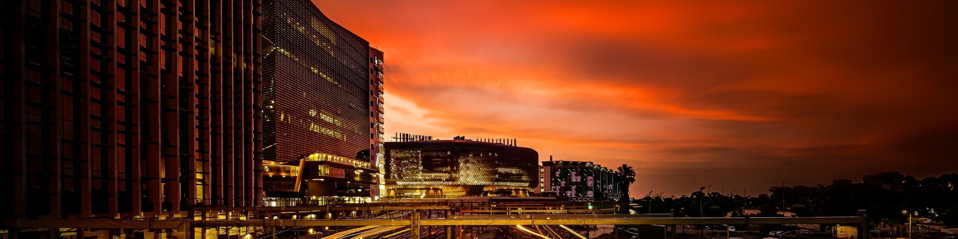 Paisagem urbana ao entardecer, com edifícios iluminados e trilhos de trem.