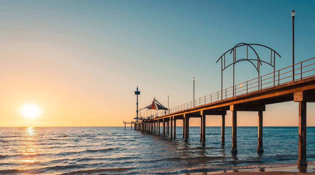 A pier extending into the sea with a sunset in the background.