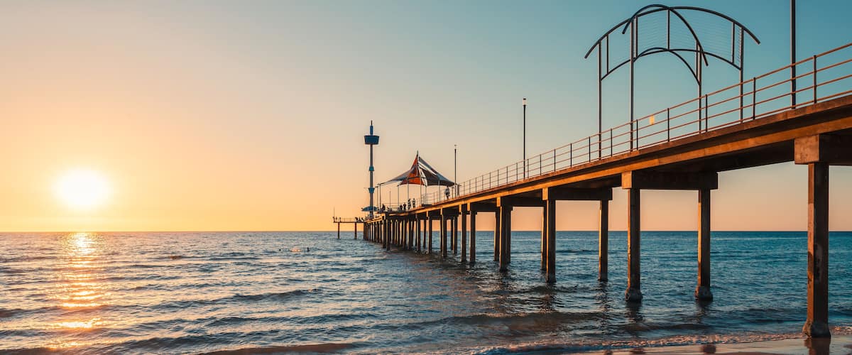 A pier extending into the sea with a sunset in the background.