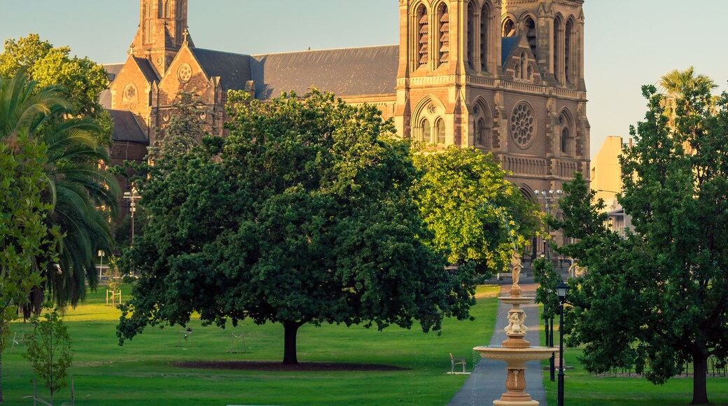 A cathedral with two prominent spires, surrounded by lush green trees and a well-maintained garden with a fountain.