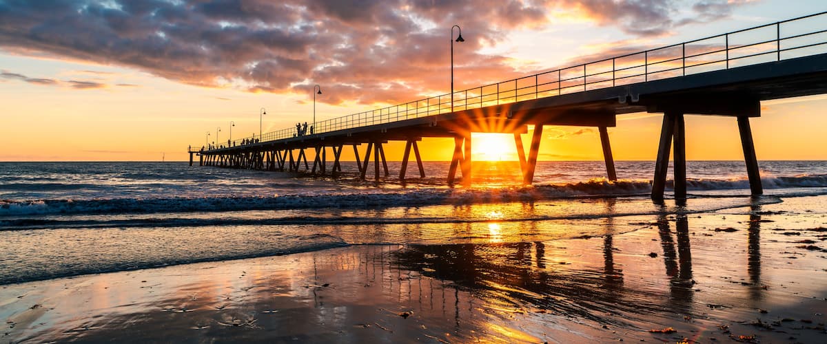 A pier extending into the ocean at sunset with the sun setting behind it.